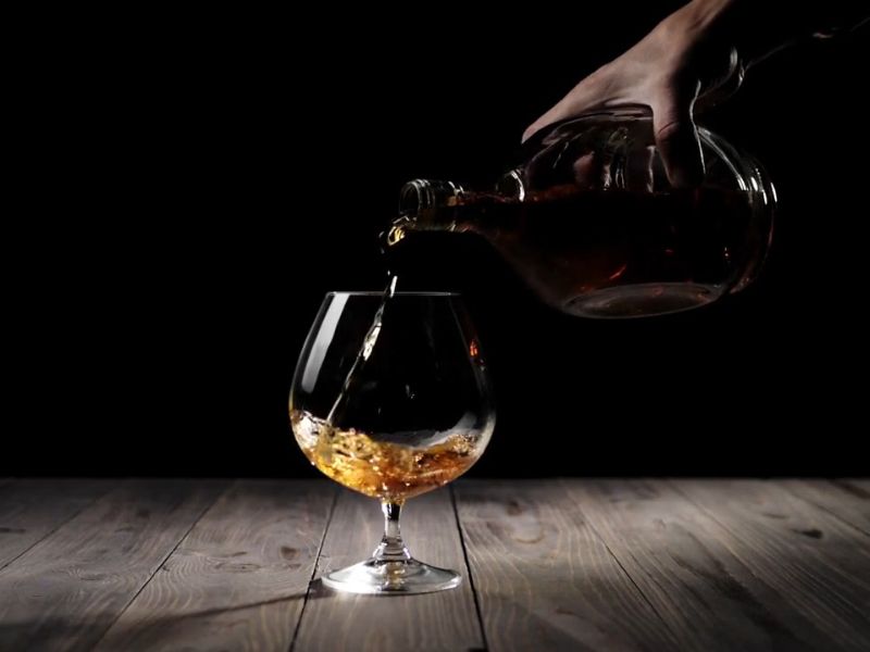 momak sipa rakiju u čašu, tamna pozadina sa prigušenim svetlom